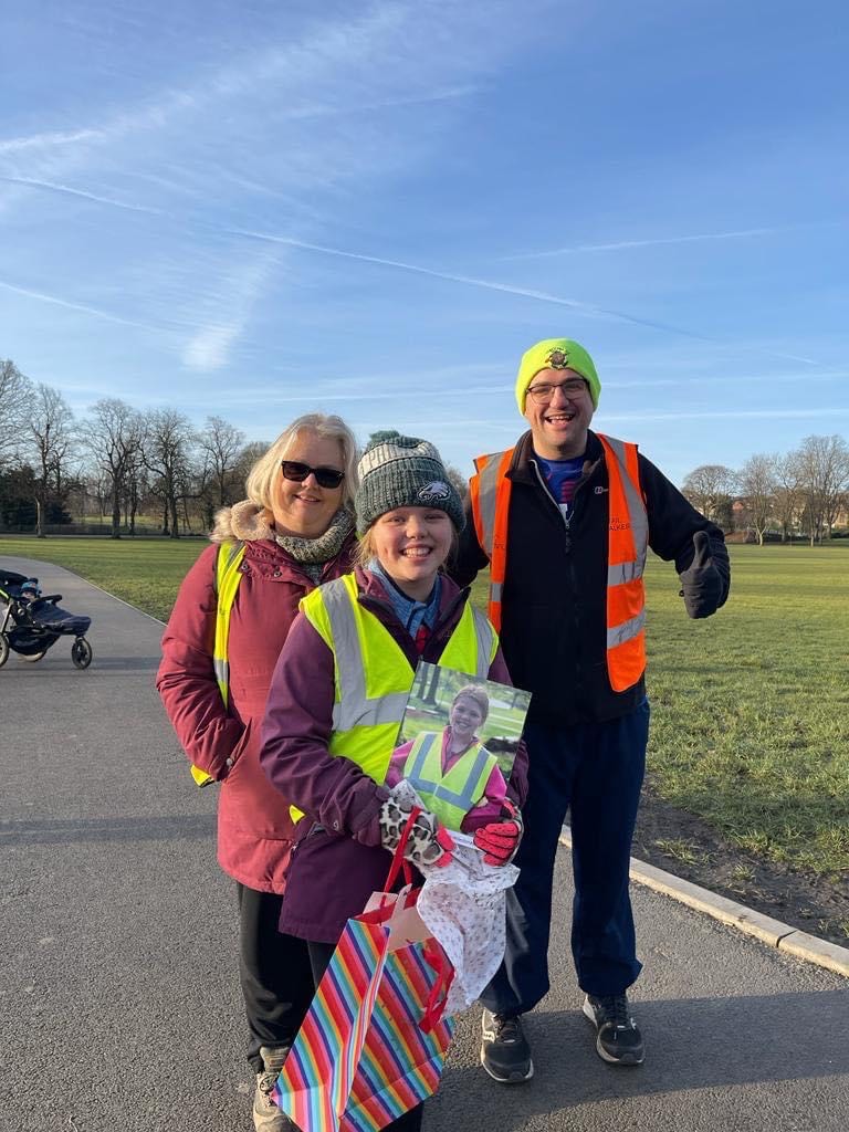 Young volunteer with her mum and dad celebrating 100 volunteering days at parkrun